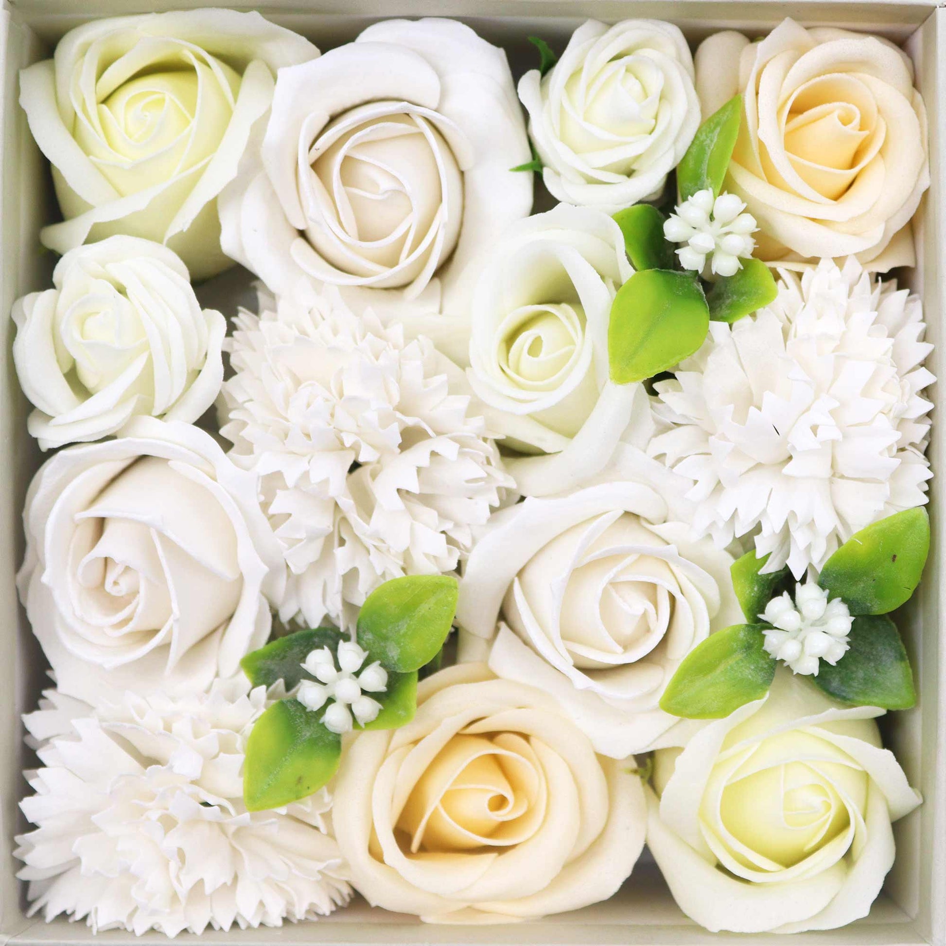 White and cream roses and carnations are arranged in a square box.  Green leaves are interspersed.