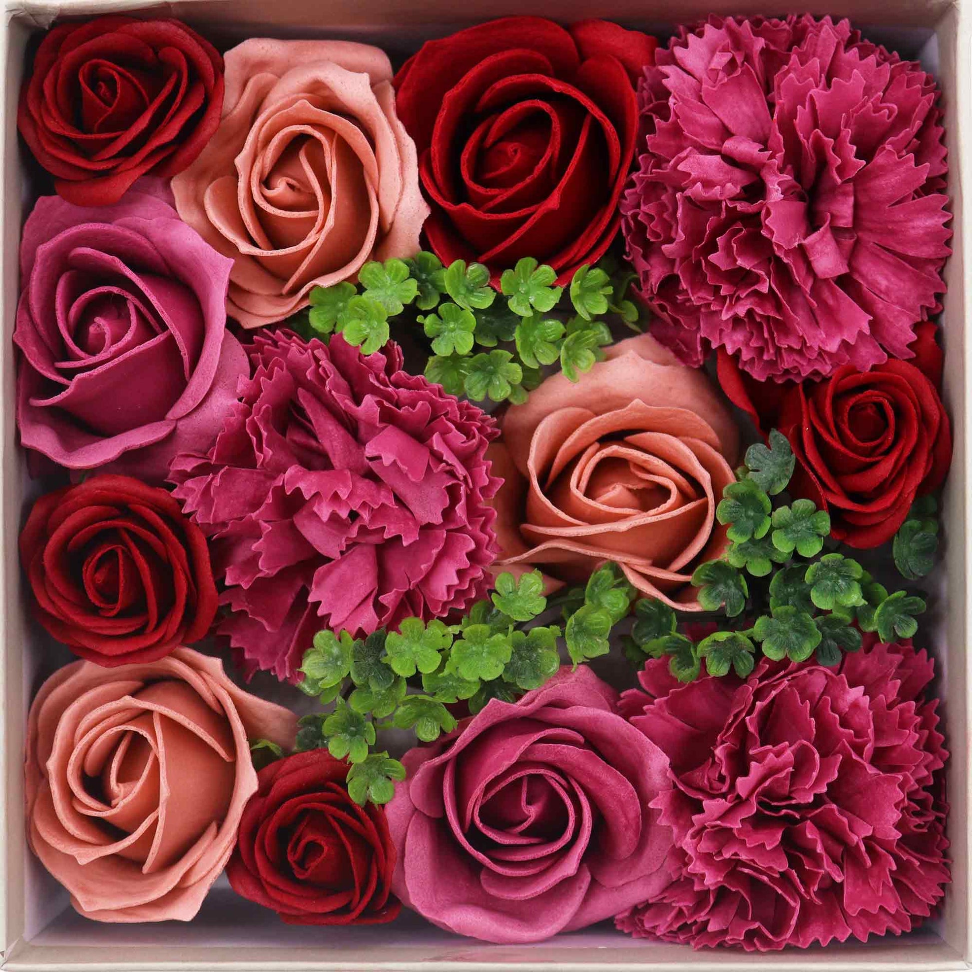 Soap roses and carnations, arranged in a box, are nestled amongst greenery.