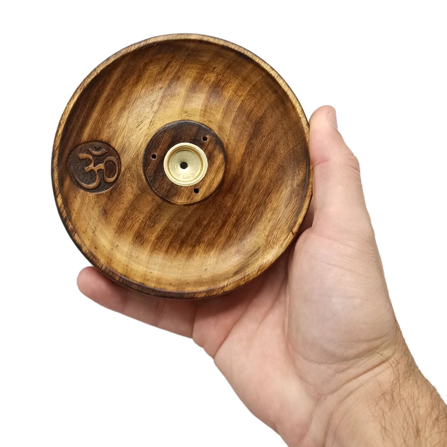 A wooden incense holder rests in a hand. It features a carved "Om" symbol and a central metal insert with holes for incense sticks.