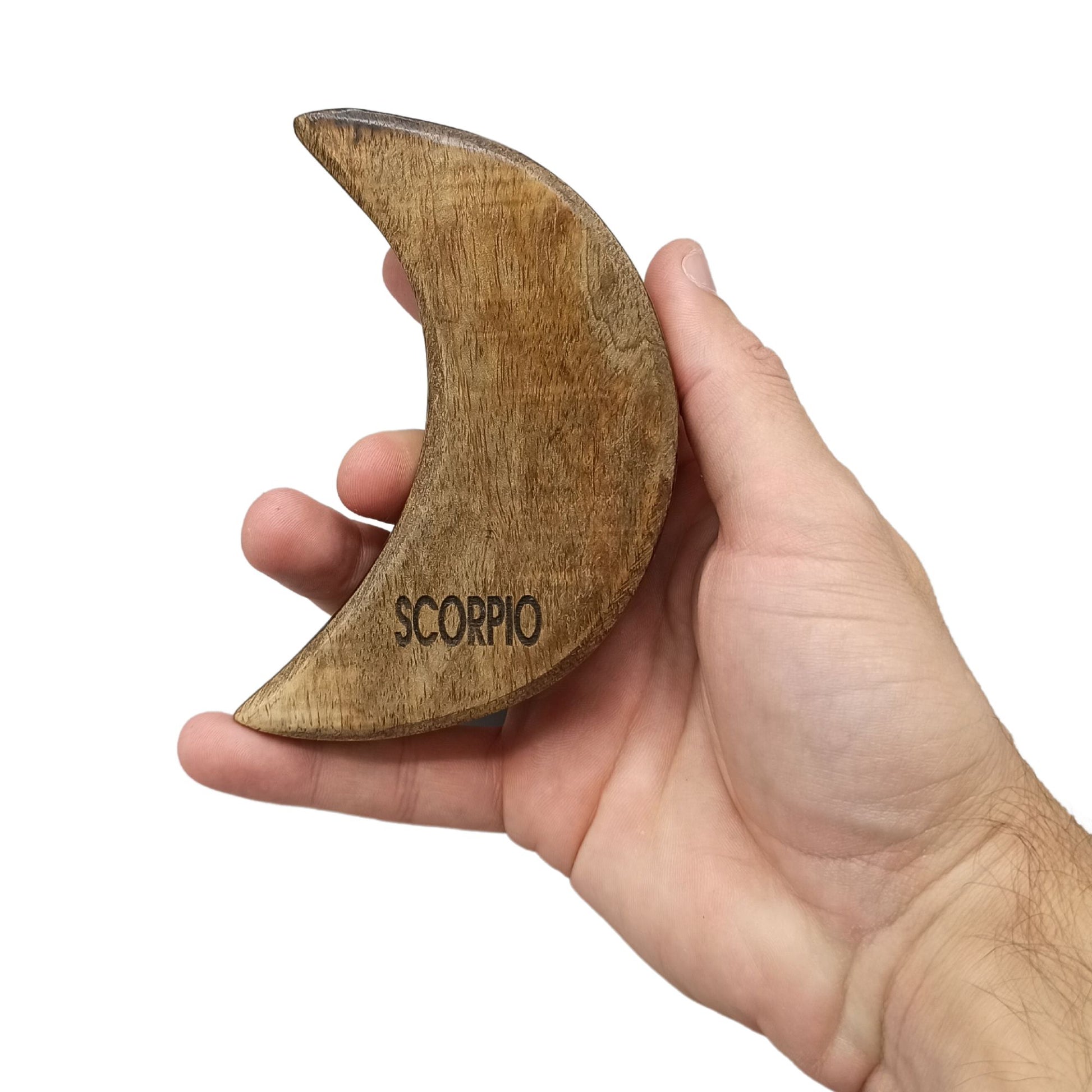 A hand holds a crescent-shaped wooden object engraved with "SCORPIO," against a plain white background, highlighting the object's natural texture and carved detail.