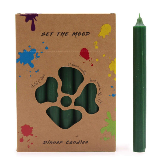 A box of green dinner candles with a floral cutout showing the candles inside sits next to a single matching candle. The box reads: "SET THE MOOD", "21 dinner candles", "Dinner Candles", "Solid Colour", "hand made in the UK". The box has colorful paint splatter designs.