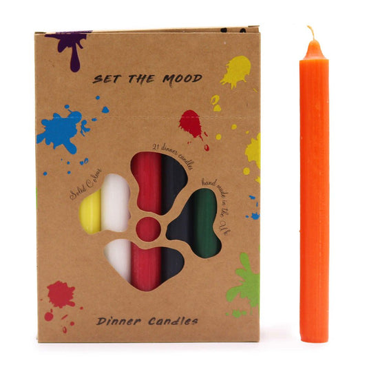 An orange candle stands next to a brown box that contains 21 dinner candles of various colors: yellow, white, red, black, and green. The box says “SET THE MOOD, Solid Colour, Dinner Candles, hand made in the UK”.