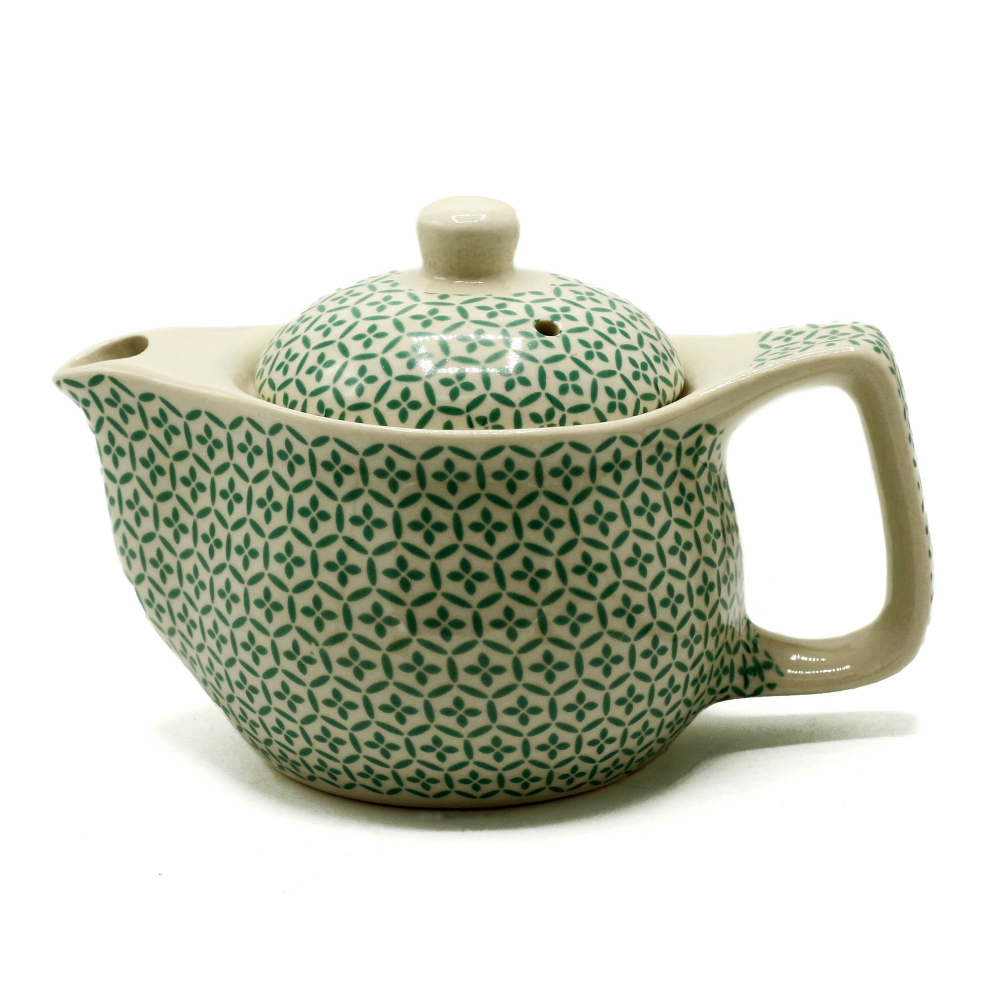 A ceramic teapot, sits on a white background. It has a beige body and a repeating green floral pattern.  The teapot has a lid and a handle.