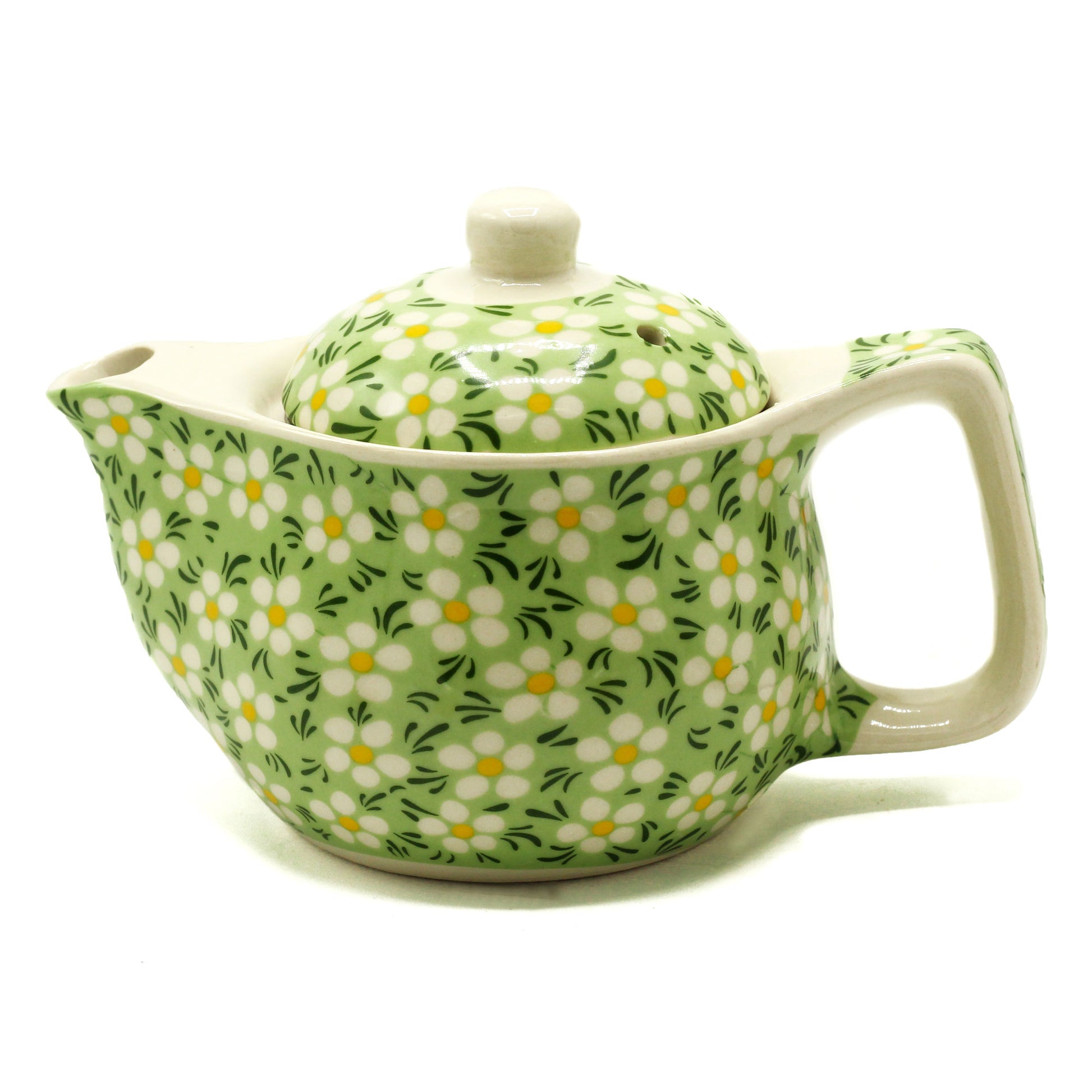 A small teapot, sits on a white background.  It is light green with a white daisy pattern, and has a matching lid.