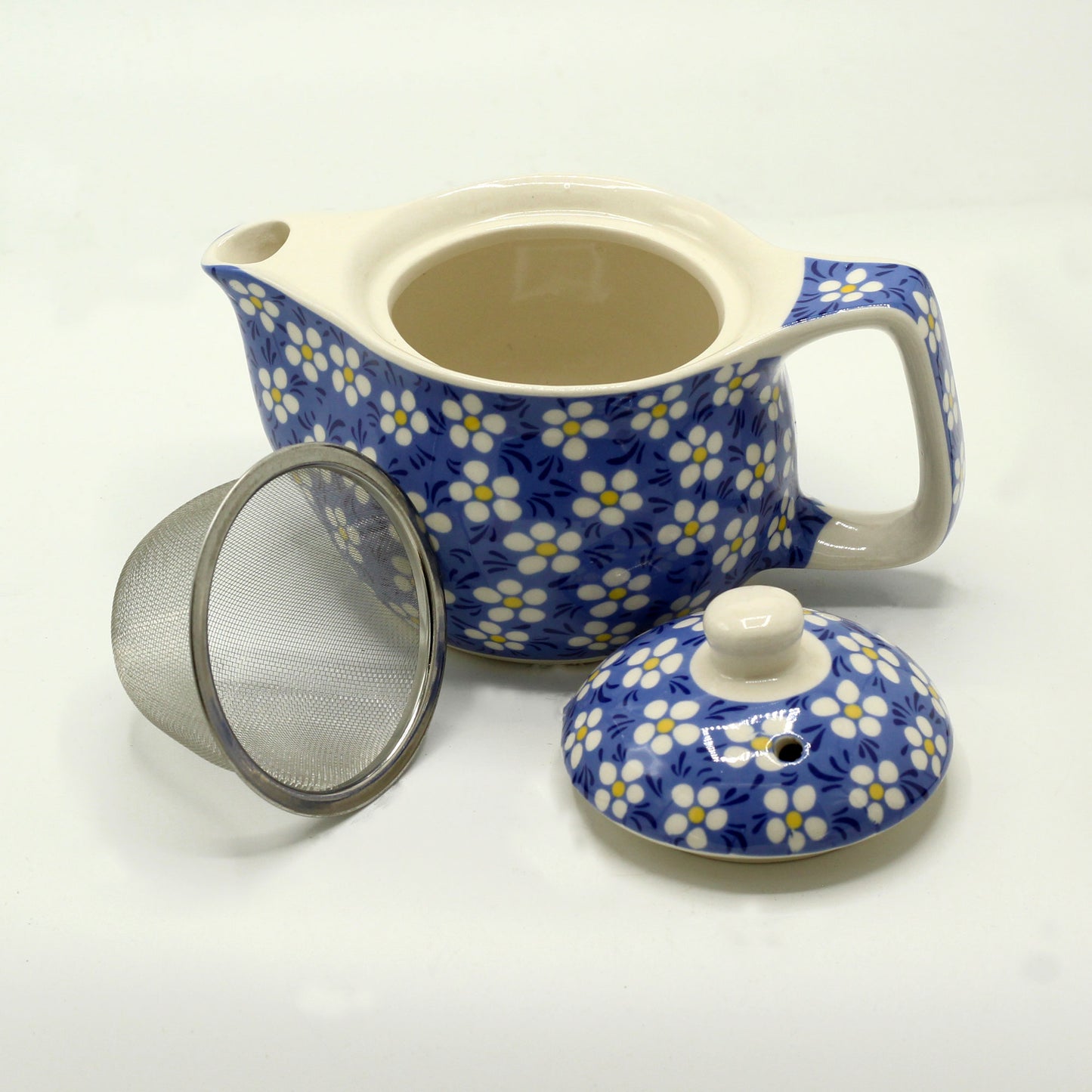 A blue and white floral teapot sits open, displaying a metal infuser and lid nearby on a white surface.