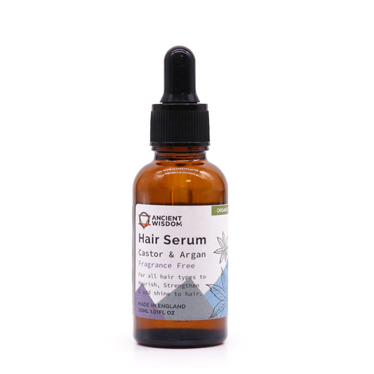 A brown glass bottle holds hair serum on a white surface. The label reads "ANCIENT WISDOM Hair Serum Castor & Argan Fragrance Free For all hair types to Nourish, Strengthen & add shine to hair. MADE IN ENGLAND 30ML 1.01FL OZ ORGANIC".