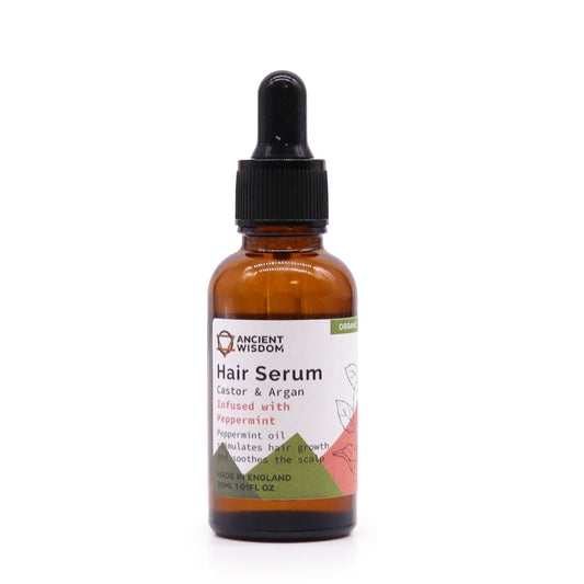 A bottle of "Ancient Wisdom Hair Serum" stands on a white surface. Text on the bottle reads, "Hair Serum, Castor & Argan, Infused with Peppermint...stimulates hair growth and soothes the scalp, MADE IN ENGLAND, 30ML 1.01FL OZ" and "ORGANIC".