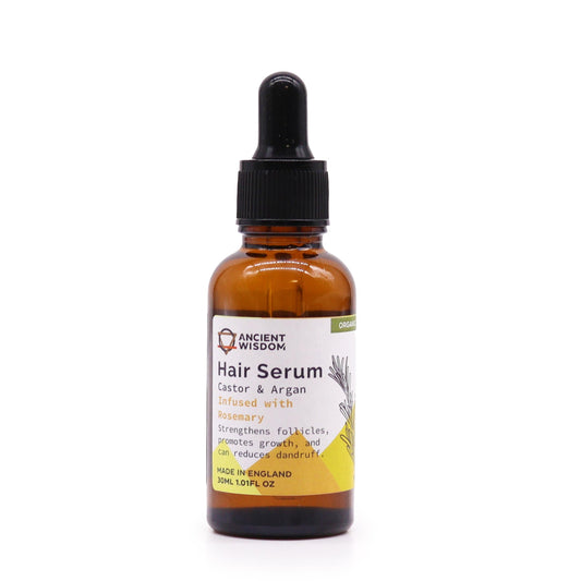 A brown glass bottle sits on a white surface. A black dropper sits on top. The bottle's label reads: "ANCIENT WISDOM, Hair Serum, Castor & Argan, Infused with Rosemary, Strengthens follicles, promotes growth, and can reduce dandruff, MADE IN ENGLAND 30ML 1.01FL OZ, ORGANIC"