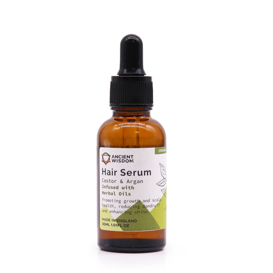 A bottle of hair serum sits on a white surface. The label reads "ANCIENT WISDOM Hair Serum Castor & Argan Infused with Herbal Oils Promoting growth and scalp health, reducing dandruff and enhancing shine. MADE IN ENGLAND 30ML 1.01FL OZ"