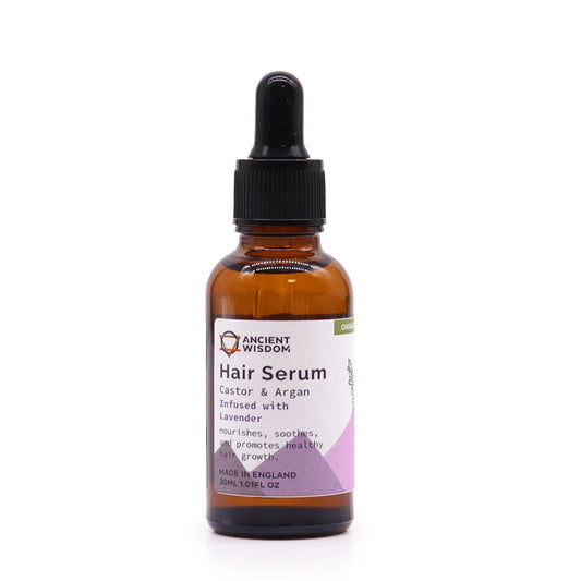 A brown glass bottle of "Ancient Wisdom Hair Serum" stands in a white space. The label reads "Castor & Argan Infused with Lavender. nourishes, soothes, and promotes healthy hair growth. MADE IN ENGLAND 30ML 1.01FL OZ".
