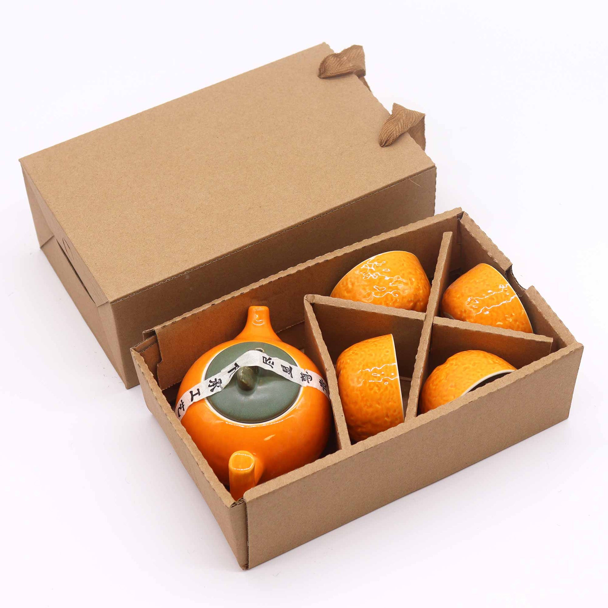 An orange ceramic teapot and four matching cups rest inside a brown cardboard box.  A ribbon with Asian characters is tied around the teapot's lid.