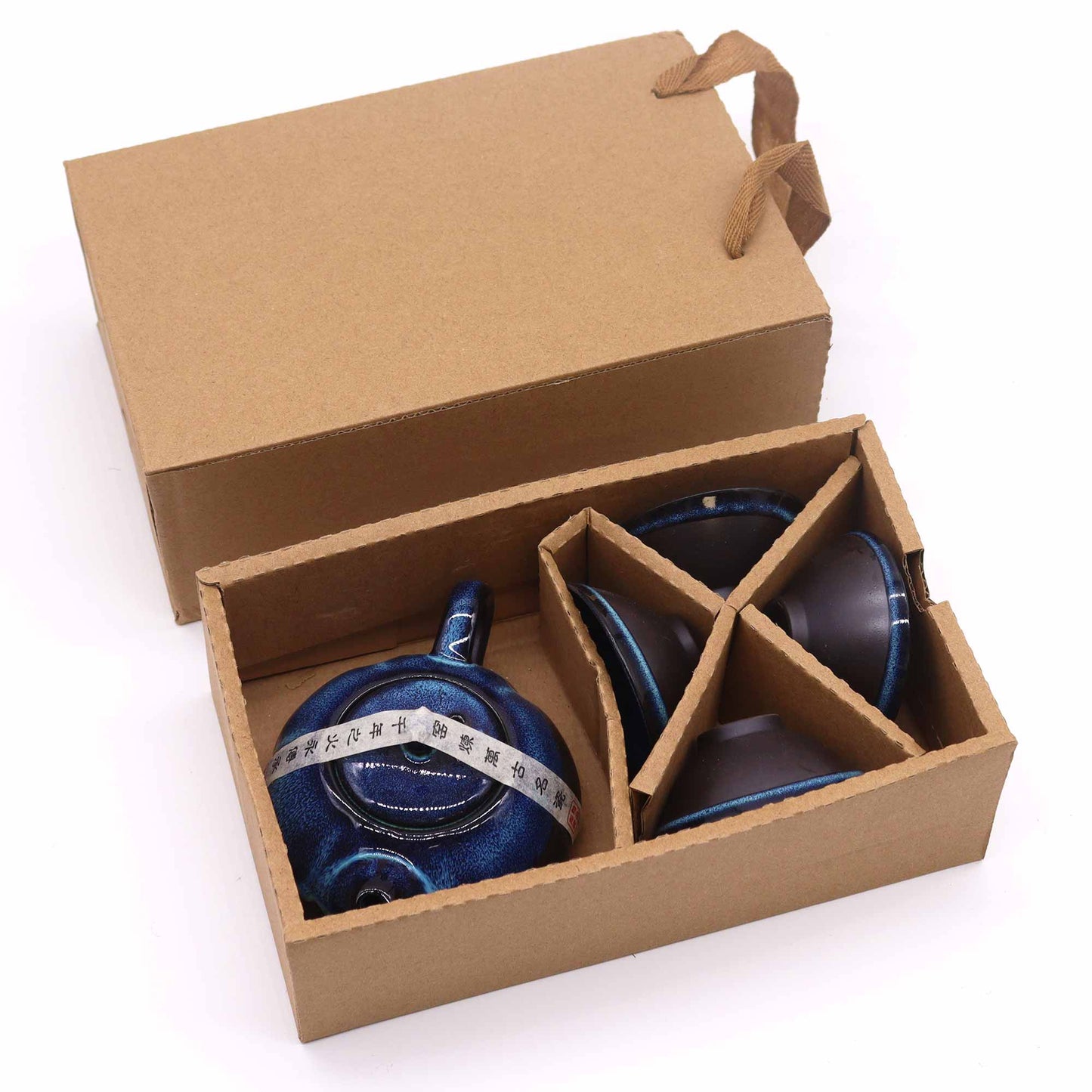 A blue ceramic teapot and cups are nestled inside a cardboard box;  the box sits on a white surface.  A label on the teapot reads:  “紫砂壶-100毫升”.