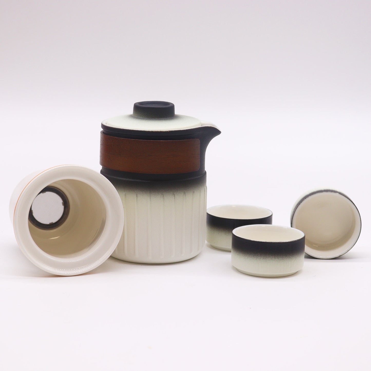 A ceramic tea set, composed of a teapot, a strainer, and three cups, sits on a white surface.  The teapot and cups are primarily white with a dark gradient base.