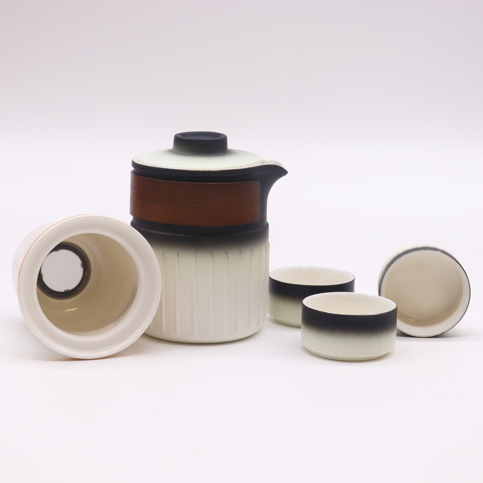 A ceramic tea set, composed of a teapot, a strainer, and three cups, sits on a white surface.  The teapot and cups are primarily white with a dark gradient base.