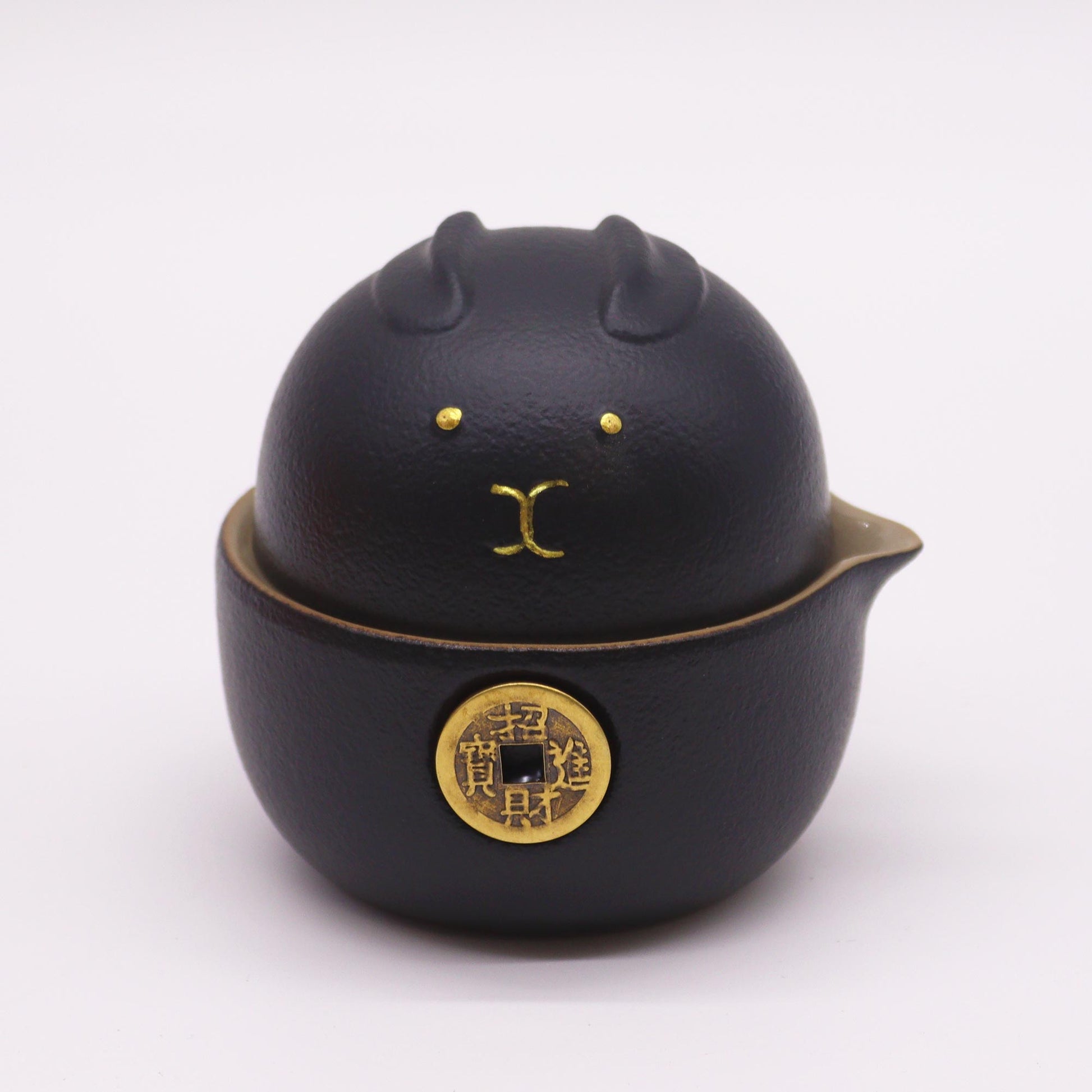A black ceramic tea infuser, shaped like a rabbit, sits on a white background.  The infuser has a small gold coin affixed to its base with Chinese characters.