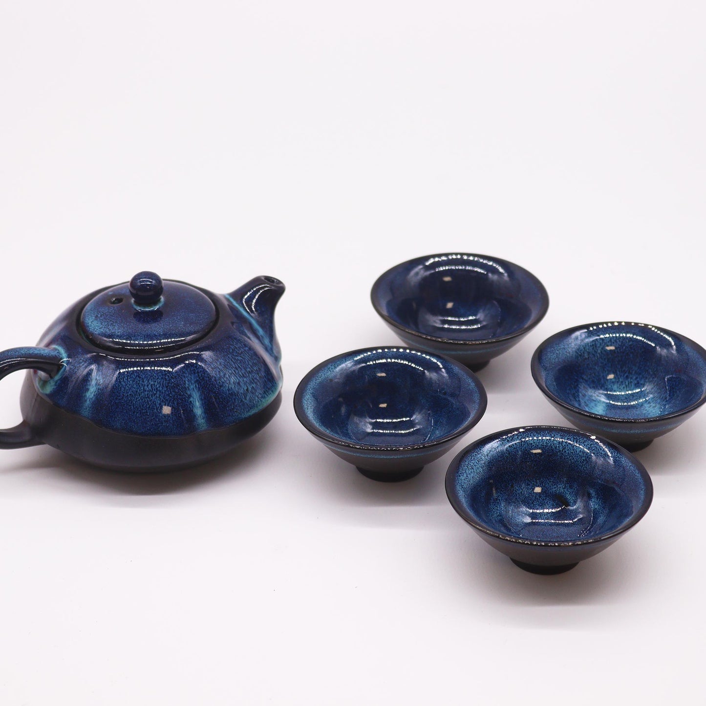 A blue ceramic teapot sits beside four matching small bowls on a white surface.