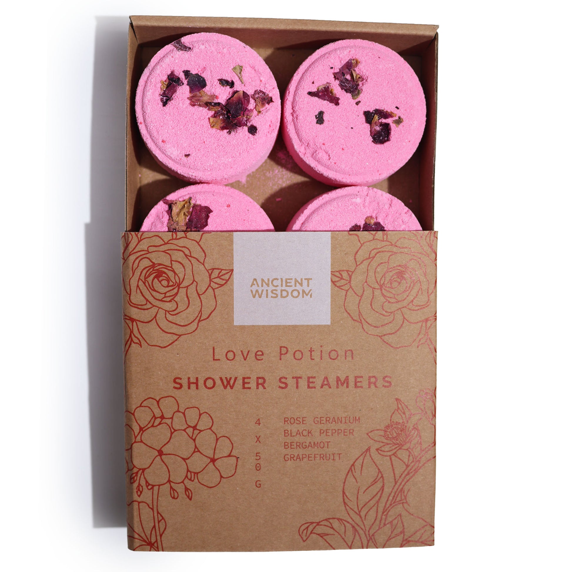 Pink shower steamers adorned with dried petals sit in a partially open cardboard box labeled "Ancient Wisdom Love Potion Shower Steamers." The box displays floral illustrations and mentions "Rose Geranium, Black Pepper, Bergamot, Grapefruit," with quantities and weight.