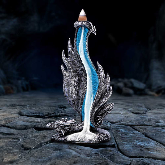 A silver dragon-shaped incense burner channels shimmering blue smoke down its sculpted wings like a cascading waterfall into a luminous pool while resting on a rough stone cave floor.