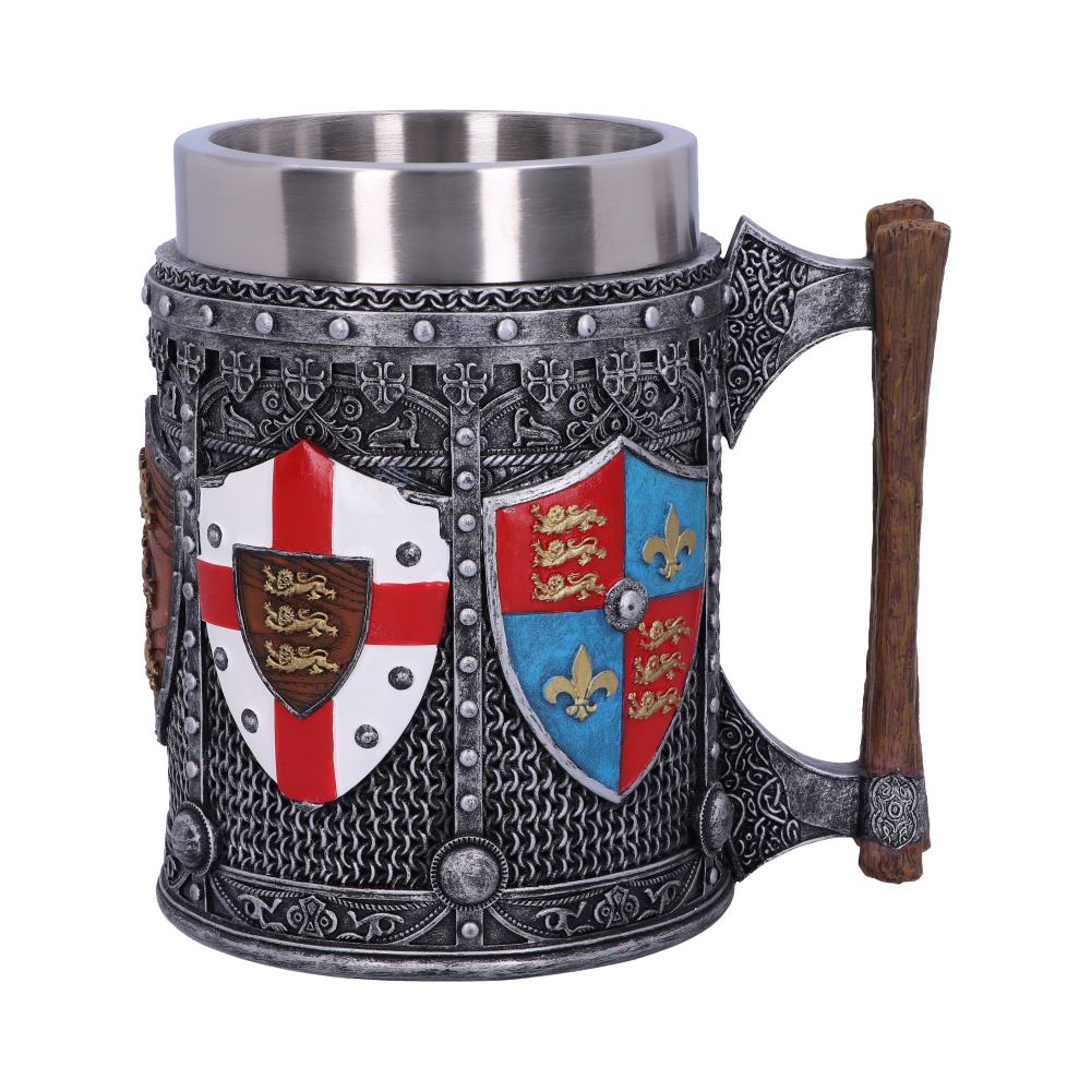 The metal mug showcases shields with heraldic symbols; one is a white shield with a red cross, another is blue and red with gold fleur-de-lis. It features a handle shaped like an axe. The background is plain white.