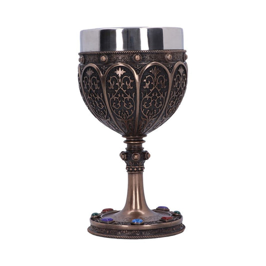 An ornate, metal chalice stands upright. The cup is detailed with patterns and a silver lip. Colored gems adorn the chalice's base. The background is plain white.