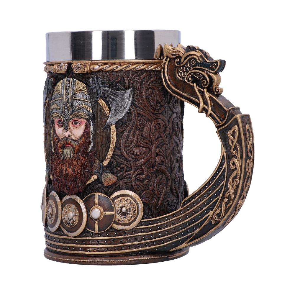 A decorative mug features Viking imagery. Its handle is a dragon head, its base mimics a longboat, and the mug's side shows a Viking warrior with axe, all in an elaborate, antique style.