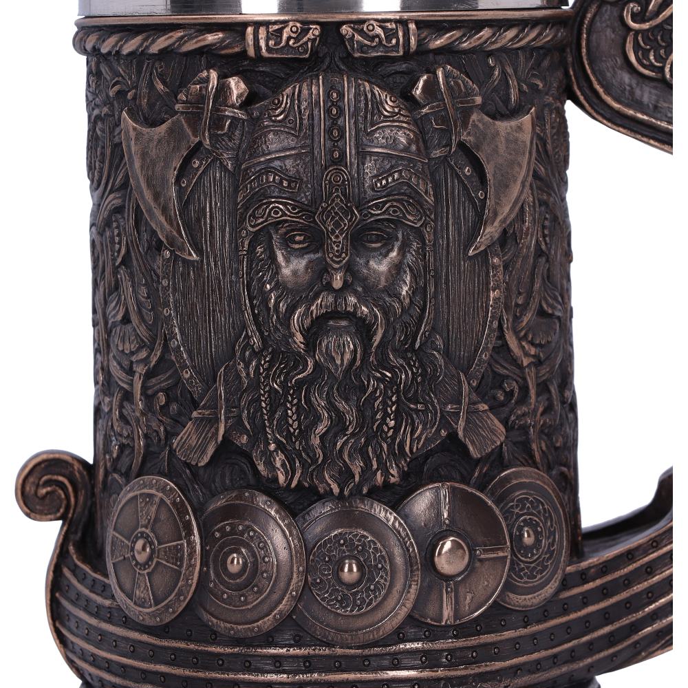 A bronze mug displays a Viking's face and a Viking boat. Shields line the bottom while axes line the top of the Viking's face.