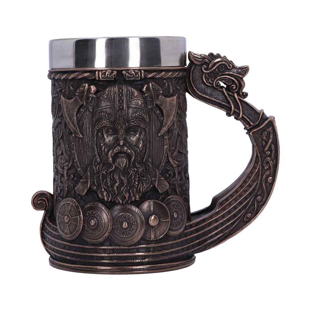 A bronze-colored mug has a metal top and a handle shaped like a Viking ship, with a dragon head at the top. The mug’s surface is carved with a Viking face, axes, and shields.