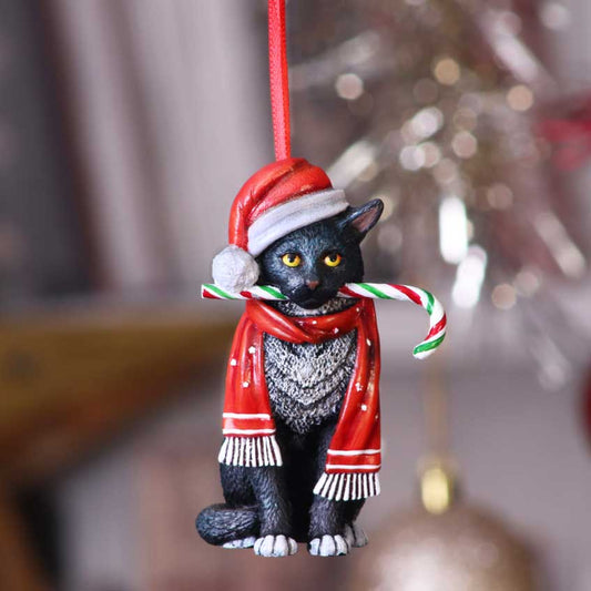 Black cat ornament hangs from a red ribbon, wearing a Santa hat and red scarf while holding a striped candy cane in its mouth against blurred holiday lights.