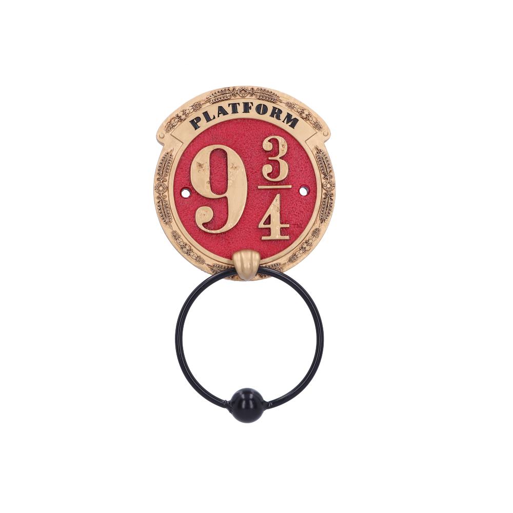 A decorative brass sign displays "Platform 9 3/4" on a red background. It features a large ring below, resembling a door knocker, set against a plain white backdrop.