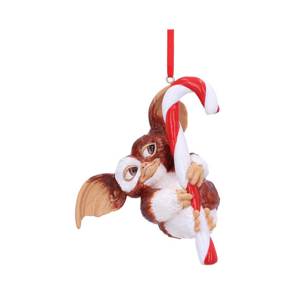 A small creature with large ears clings to a red-and-white candy cane ornament, suspended from a red string, set against a plain white background.