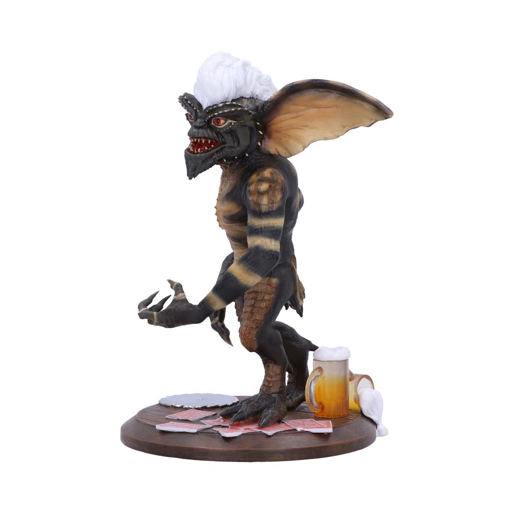 A gremlin-like creature with large ears and white hair stands on a circular base. It is surrounded by scattered playing cards and a mug of frothy beer, indicating a playful, mischievous setting.