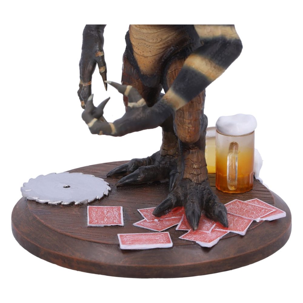 A dinosaur figure holds a saw blade on a round wooden base, surrounded by scattered playing cards and a frothy mug of beer.