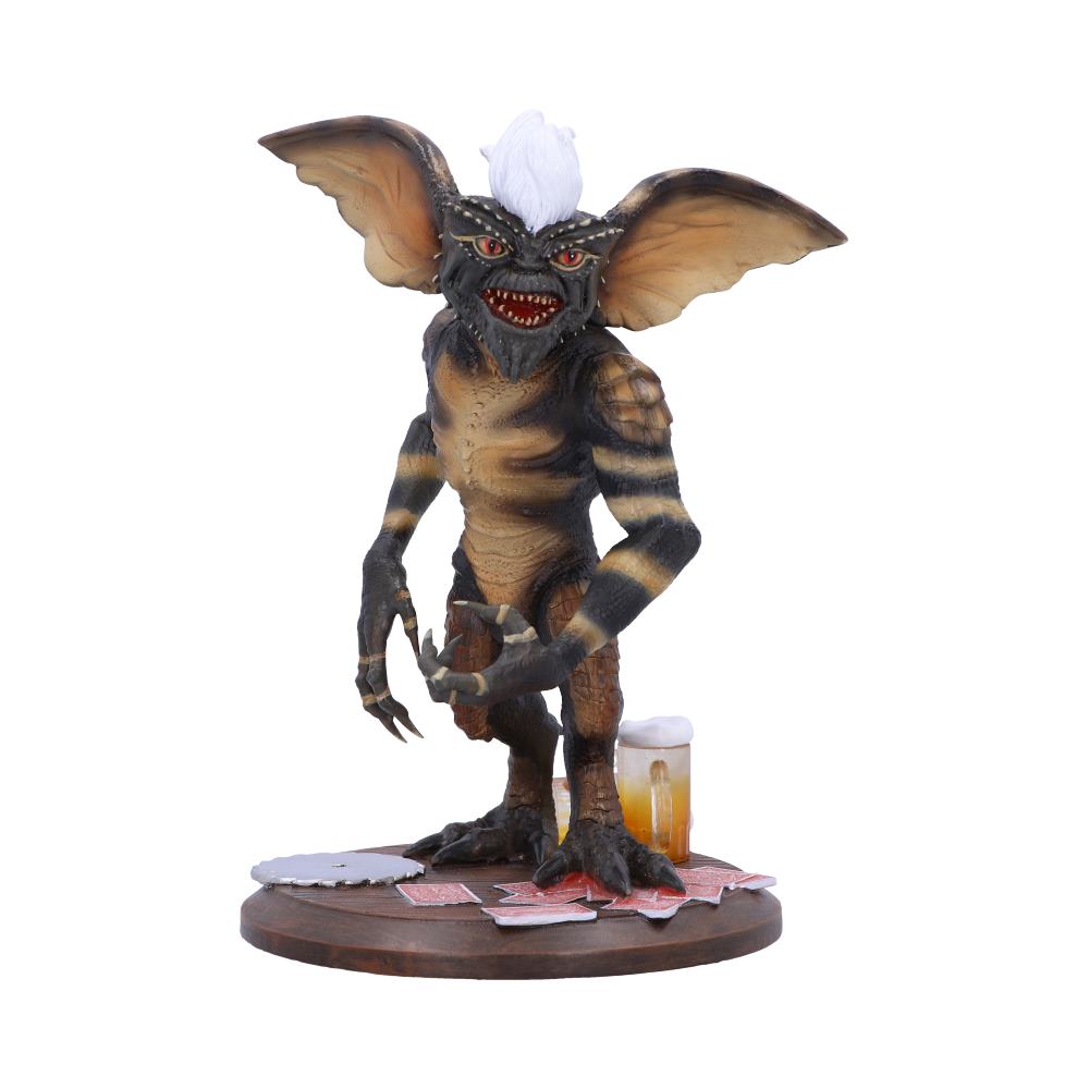 A gremlin-like figure with large ears and white hair stands menacingly on a circular base covered with playing cards and a beer mug, evoking a mischievous atmosphere.