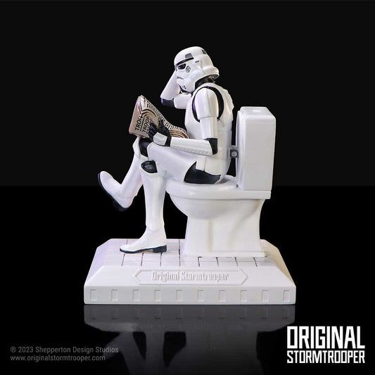 Stormtrooper figurine sits on a toilet reading a newspaper against a black background; visible text: "Original Stormtrooper", "© 2023 Shepperton Design Studios", "www.originalstormtrooper.com", "ORIGINAL STORMTROOPER", "TROOP".