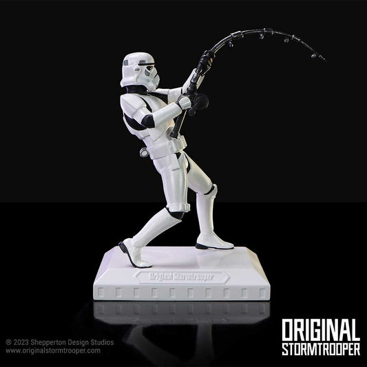 Stormtrooper figurine pulling a curved grappling line on a white display base against a black reflective background; text on base: "Original Stormtrooper"; lower right: "ORIGINAL STORMTROOPER"; lower left: "© 2023 Shepperton Design Studios www.originalstormtrooper.com"