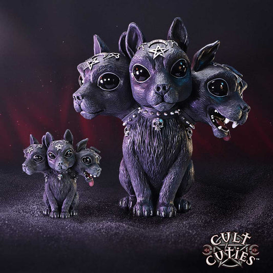 Three-headed black dog figurine sits forward-facing on a textured dark surface, a miniature twin beside it, in a moody red-black backdrop, adorned with pentagrams and skull collar; text: CULT CUTIES™