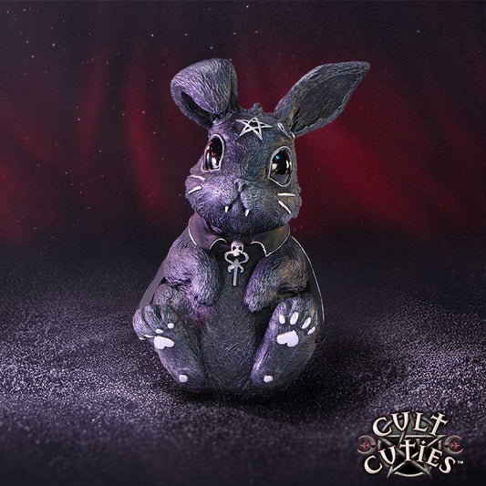 Gothic black bunny figurine sits facing forward, adorned with a forehead pentagram and skull ankh pendant, on a speckled dark surface against a red and black backdrop; text 'CULT CUTiES™'.