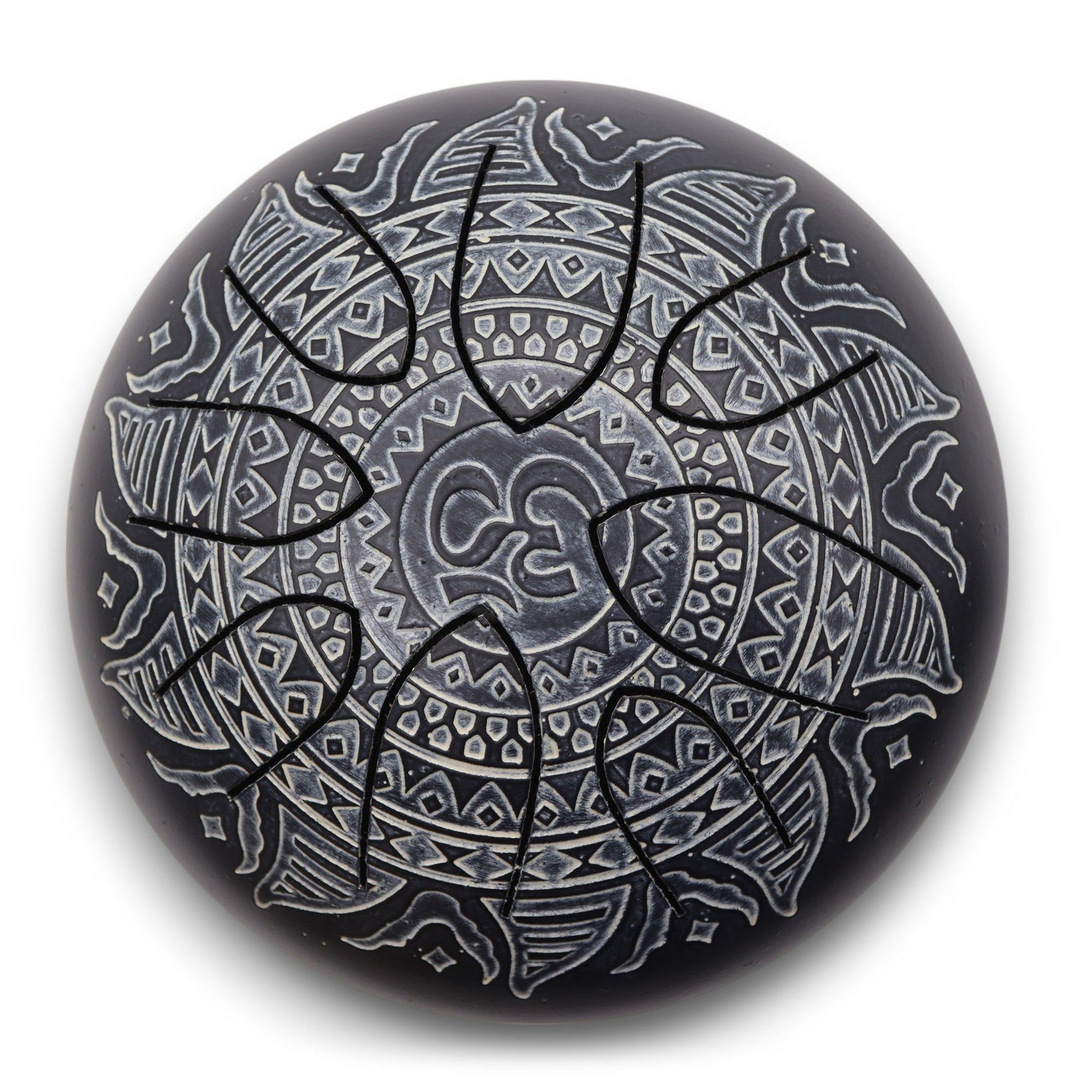 Round black steel tongue drum features eight radial cut tongues and a carved white-painted mandala with a central Om symbol, photographed on a white surface with soft shadow.