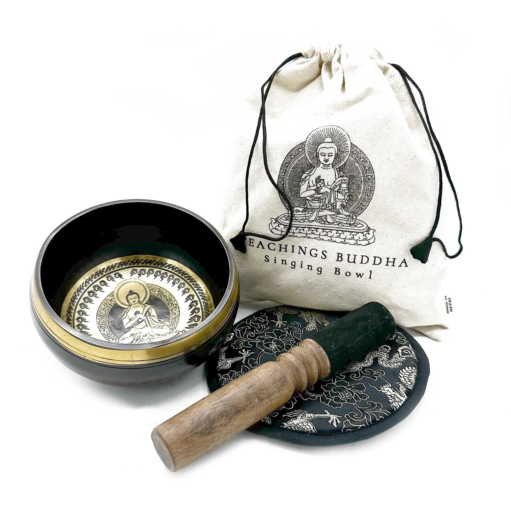 Brass Tibetan singing bowl sits open with a wooden striker on a patterned cushion beside a drawstring canvas bag on a white surface; text on bag: "EACHINGS BUDDHA Singing Bowl" and "MADE IN NEPAL".