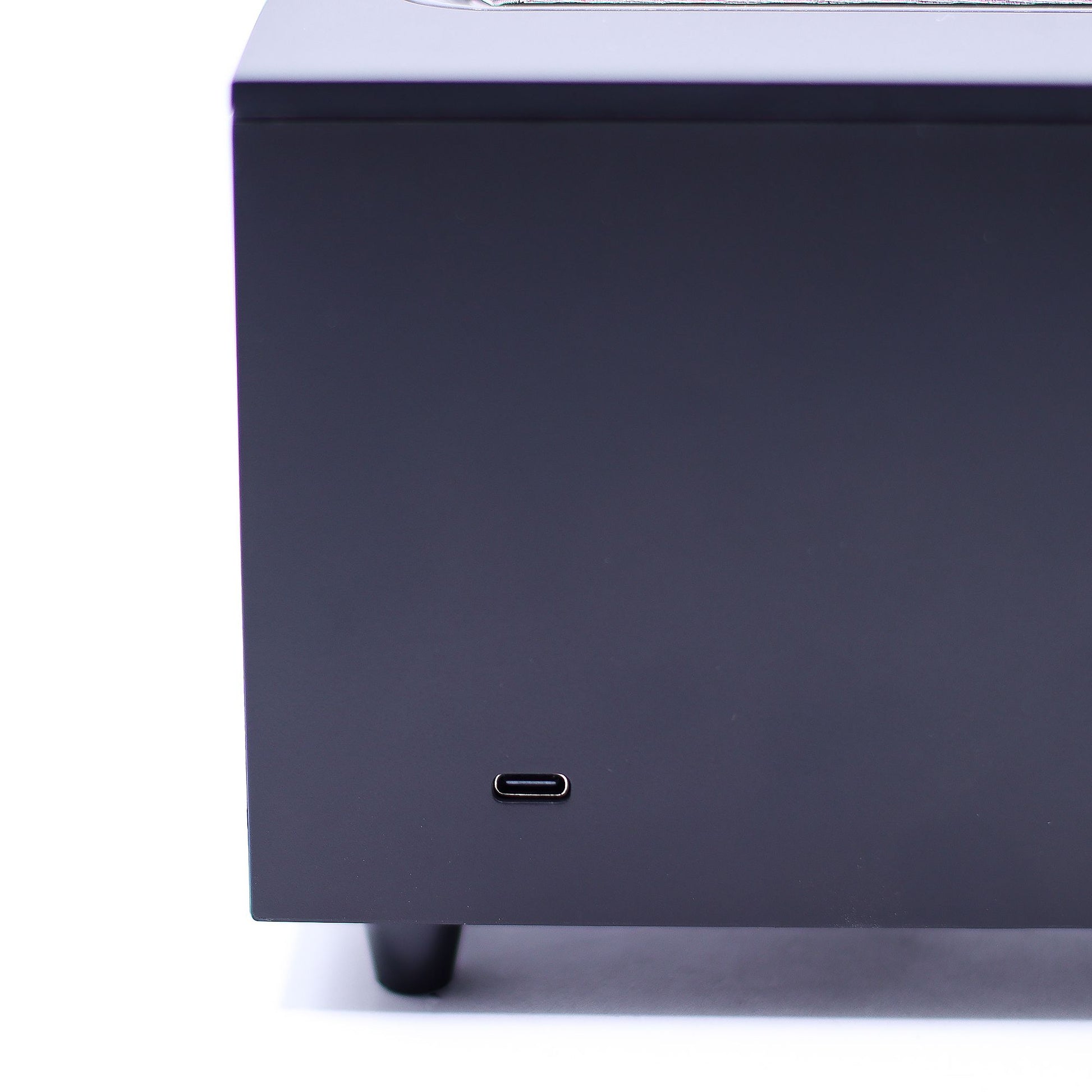 Dark gray rectangular electronics enclosure shows a USB-C port centered near its lower front face, sitting on small black feet against a white background.