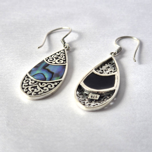 Teardrop silver earrings display abalone inlay and filigree, lying on a white surface; back of one shows stamp 925.