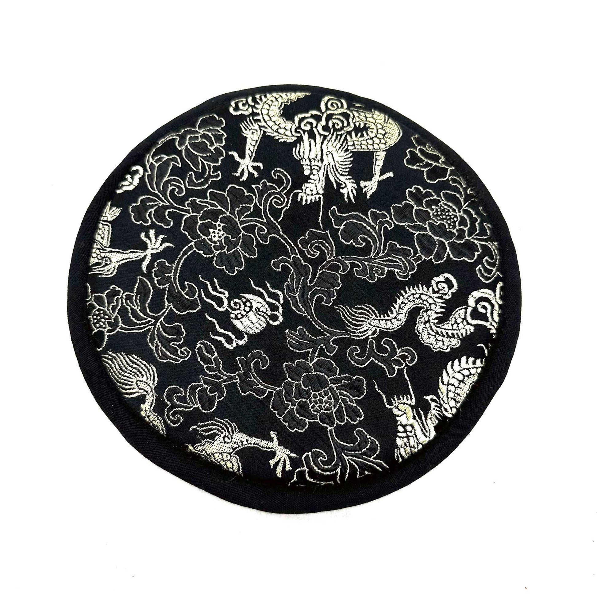 Round black silk coaster features silver embroidered dragons and peony flowers lying flat on a white surface.