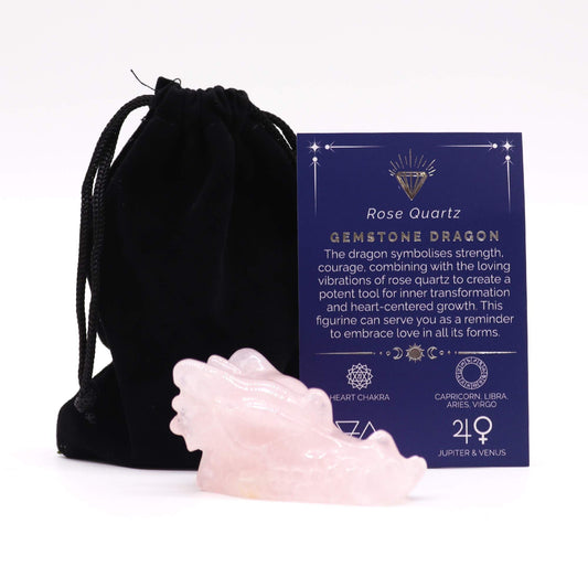 Rose quartz dragon figurine sits before a black velvet drawstring pouch and a blue informational card in studio lighting; Text on card: Rose Quartz GEMSTONE DRAGON The dragon symbolises strength, courage, combining with the loving vibrations of rose quartz to create a potent tool for inner transformation and heart-centered growth. This figurine can serve you as a reminder to embrace love in all its forms. HEART CHAKRA CAPRICORN, LIBRA, ARIES, VIRGO JUPITER & VENUS