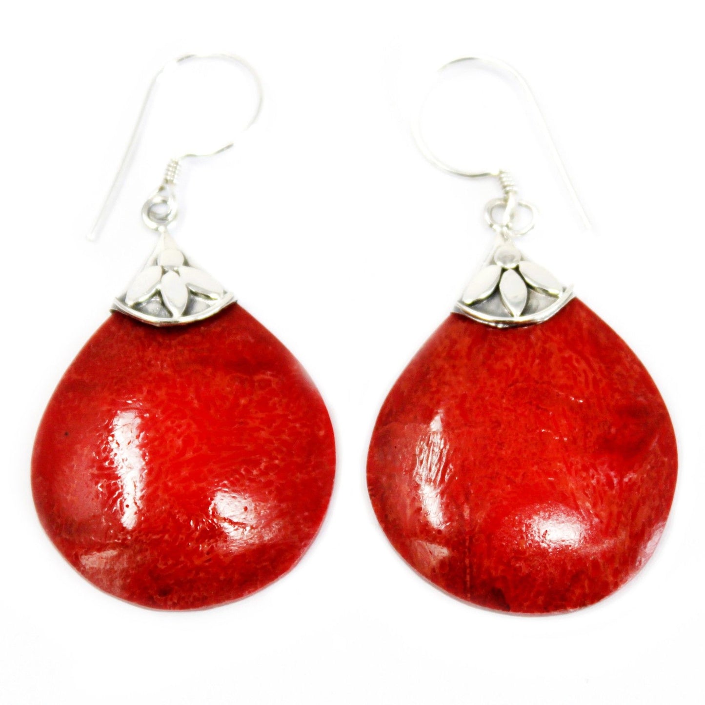 Pair of red teardrop earrings hanging from silver hook findings, showing glossy textured coral like surfaces and small silver floral caps against a plain white background.