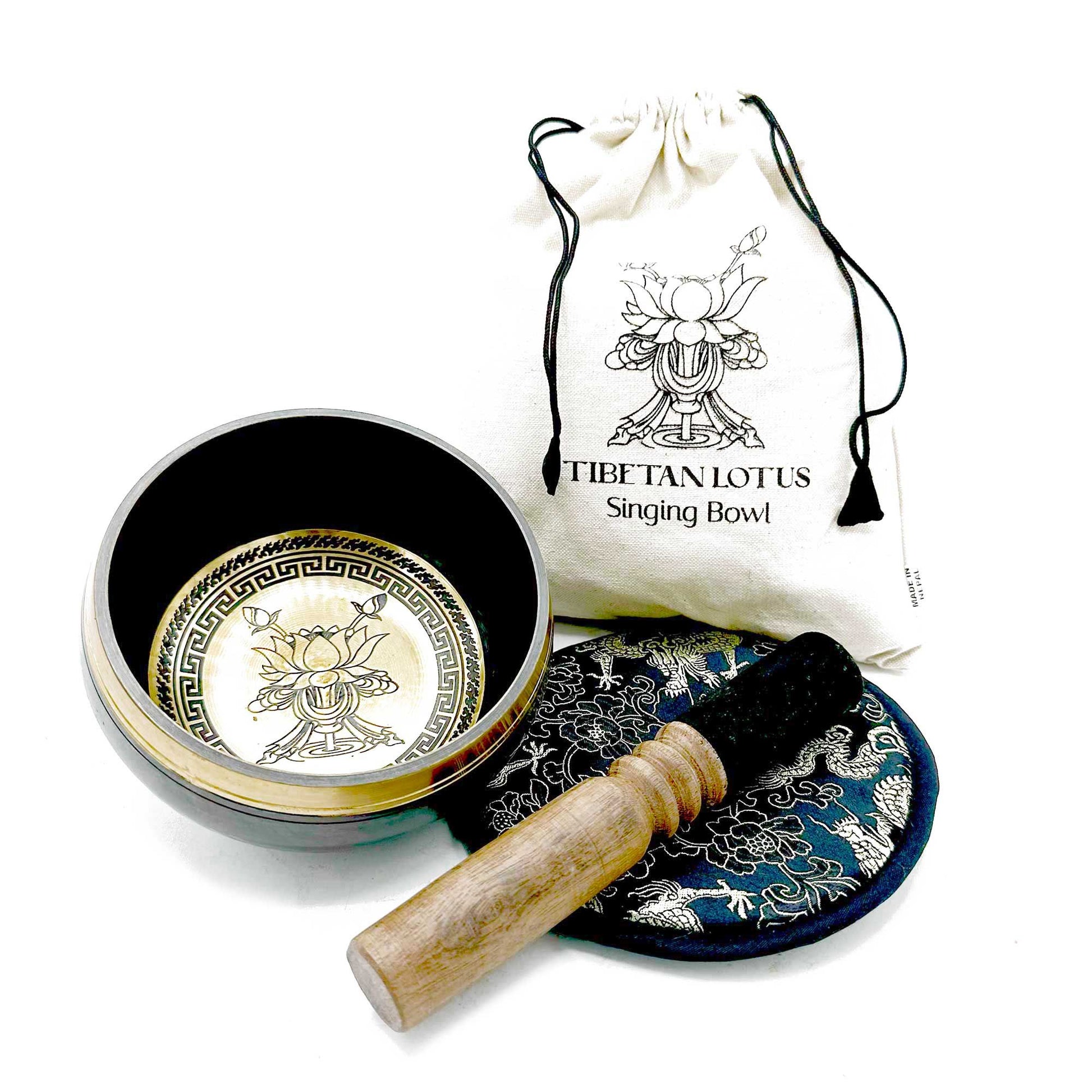 Tibetan singing bowl sits open displaying etched lotus design, wooden striker rests on embroidered cushion, beside a cloth drawstring bag printed TIBETAN LOTUS Singing Bowl on a white background.