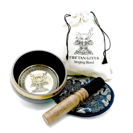 Tibetan singing bowl sits open displaying etched lotus design, wooden striker rests on embroidered cushion, beside a cloth drawstring bag printed TIBETAN LOTUS Singing Bowl on a white background.