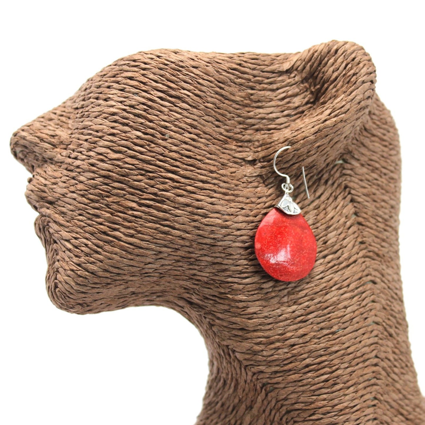 Red teardrop earring hangs from the ear of a brown woven-fiber mannequin head displayed against a white background.