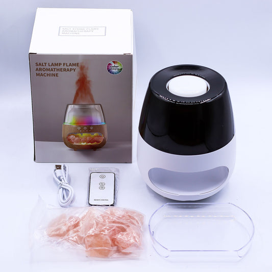 Salt lamp flame aromatherapy machine sits beside its box, USB cable, remote, plastic tray and bag of pink salt on a white surface; box reads "SALT LAMP FLAME AROMATHERAPY MACHINE", top reads "SALT STONE FLAME AROMATHERAPY MACHINE", logo reads "color changing", remote reads "REMOTE CONTROL".