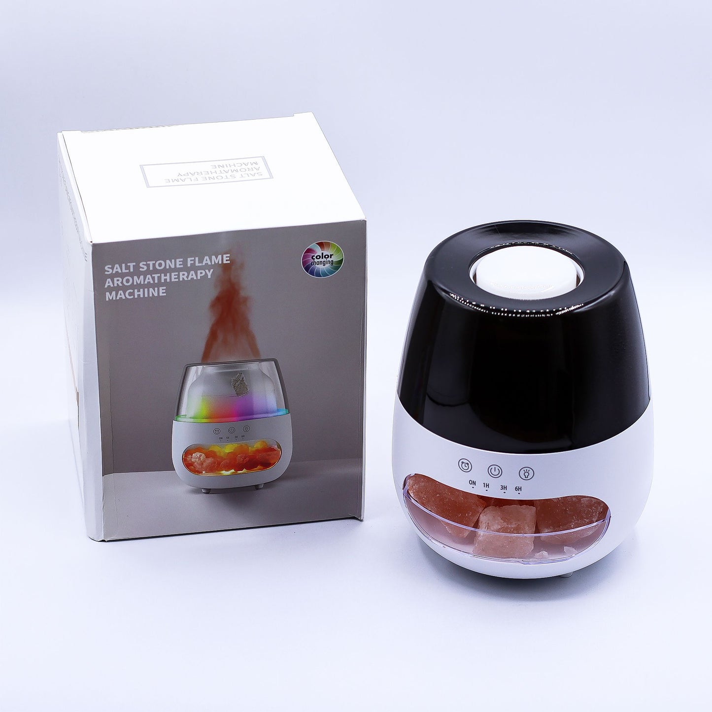 Salt stone flame aromatherapy machine sits beside its retail box on a white surface, showing pink salt crystals inside; box text reads SALT STONE FLAME AROMATHERAPY MACHINE and color changing; product front reads ON 1H 3H 6H