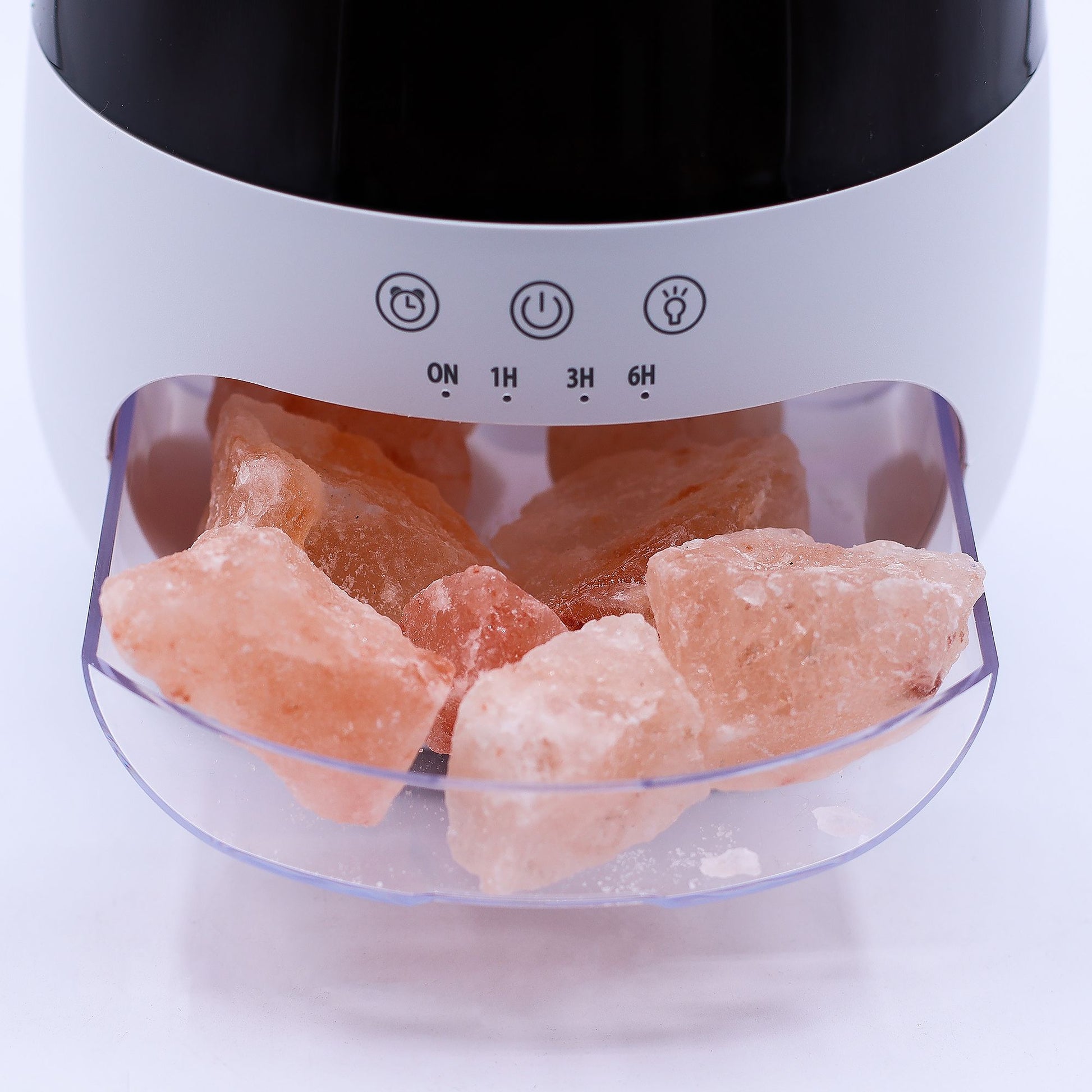 Himalayan pink salt chunks rest in a clear front drawer of a white tabletop diffuser showing control symbols and the label ON 1H 3H 6H on a white surface.
